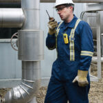 Worker using gas monitor and radio near pipeline, highlighting the importance of gas monitoring in industrial settings.