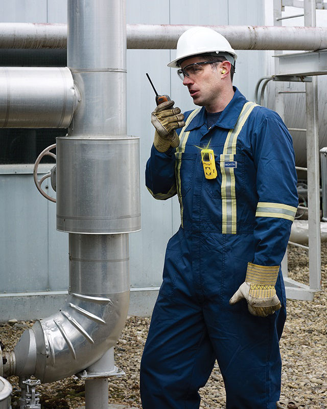 Worker using gas monitor and radio near pipeline, highlighting the importance of gas monitoring in industrial settings.
