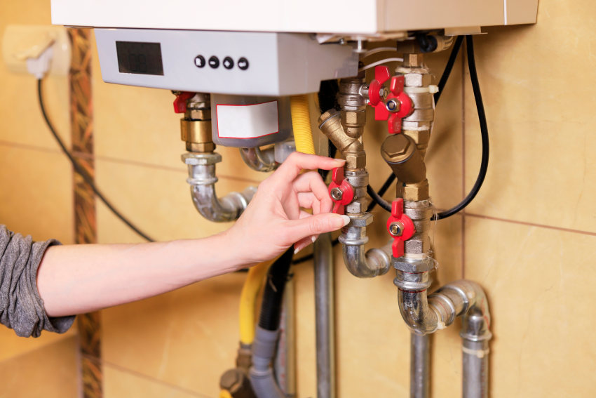 Person adjusts red gas valve on a gas system, illustrating inspection steps in gas safety audits for compliance.