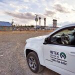 Hetek Solutions Inc. pipeline inspection vehicle parked at an industrial site with gas facility and storage towers in the background under a cloudy sky