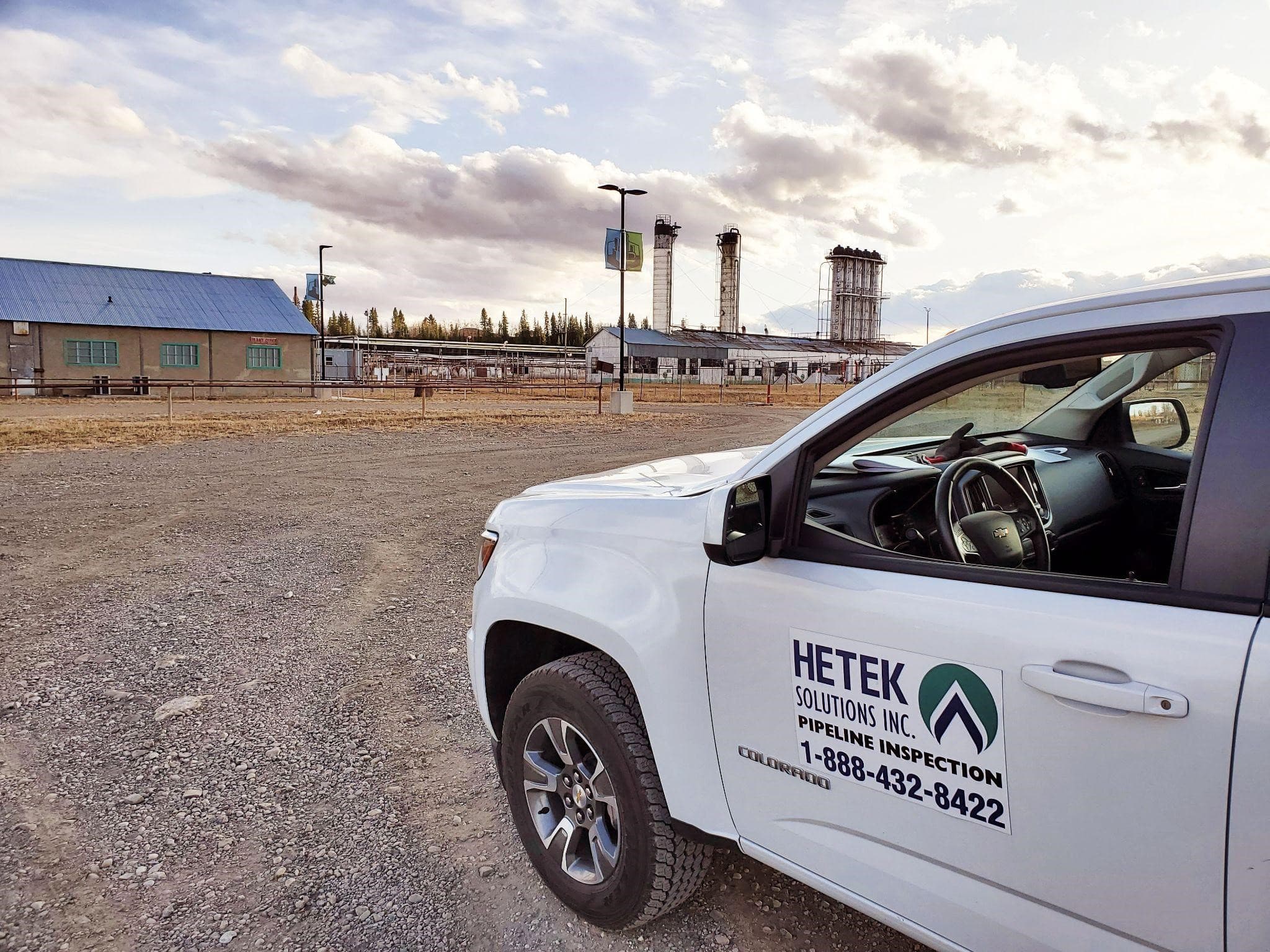 Hetek Solutions Inc. pipeline inspection vehicle parked at an industrial site with gas facility and storage towers in the background under a cloudy sky